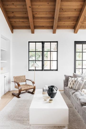 Rustic modern living room with exposed wood beam ceiling, white walls, and natural earth-tone furnishings