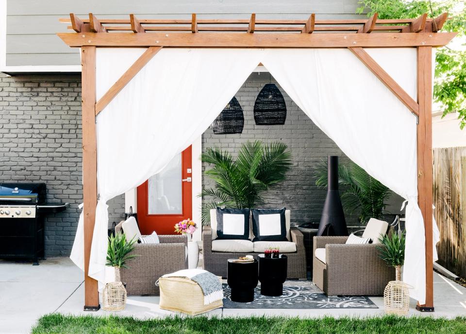 Contemporary pergola seating area with warm wood frame, neutral tones, woven accents, and modern outdoor furnishings.