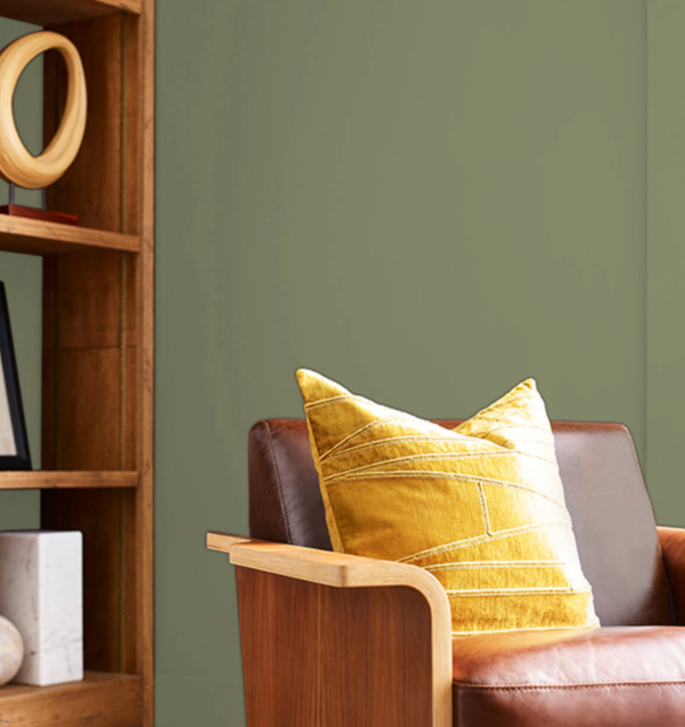 Warm sage green wall paired with mid-century wood furnishings and golden yellow accent pillow for balanced, sophisticated comfort