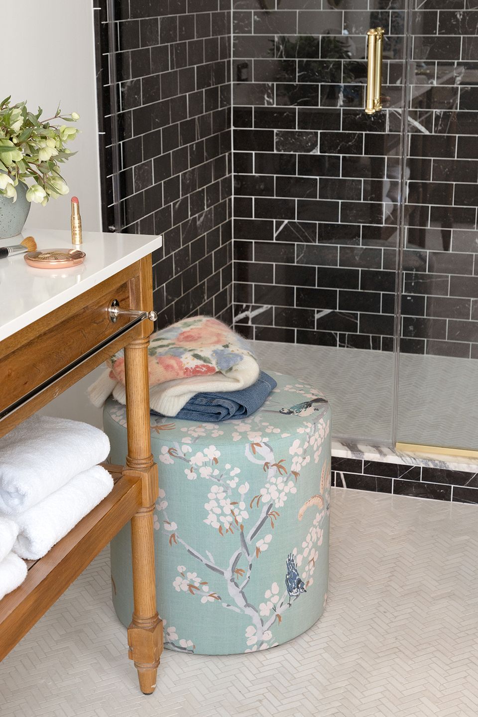 Eclectic bathroom blending black subway tile with warm wood vanity and floral ottoman