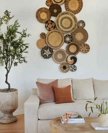 Minimalist living room with woven basket wall art, cream linen sofa, terracotta pillows, and potted plant emphasizing organic natural textures
