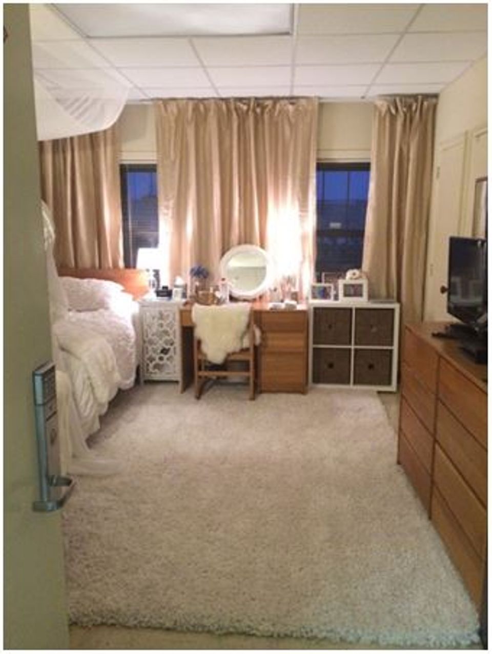 Warm, layered dorm with canopy bed, neutral linen curtains, wooden furniture, and organized vanity setup