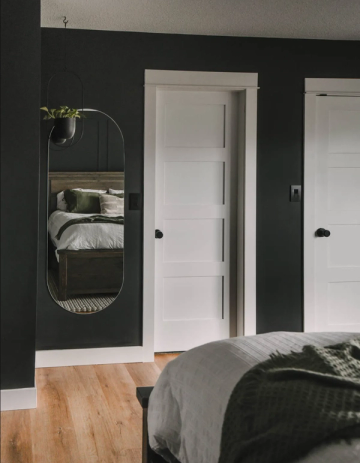 Modern bedroom with charcoal walls, white trim doors, brass oval mirror, and natural wood flooring establishing dramatic, sophisticated sanctuary aesthetic