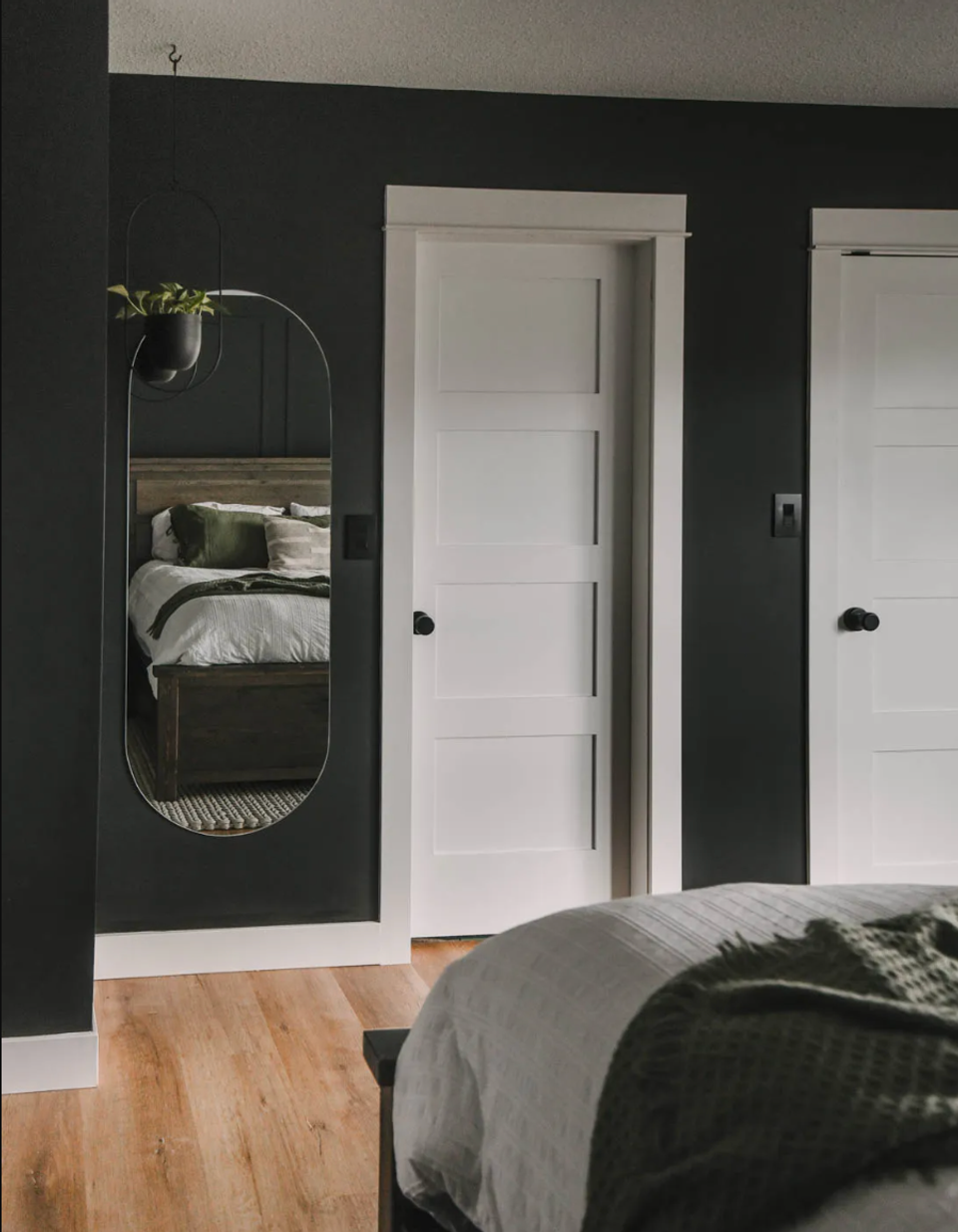 Modern bedroom with charcoal walls, white trim doors, brass oval mirror, and natural wood flooring establishing dramatic, sophisticated sanctuary aesthetic