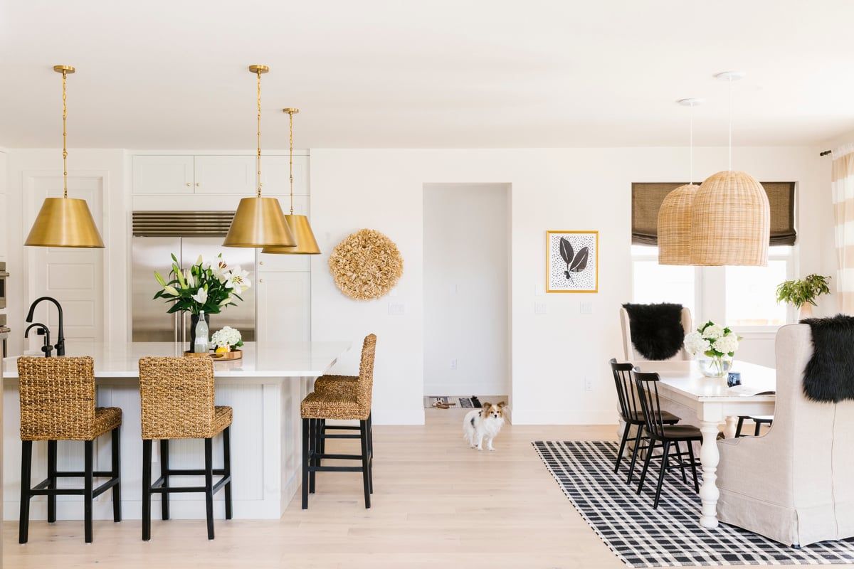 Bright, airy coastal-modern kitchen and dining space with natural woven accents, brass pendant lights, and black-and-white geometric rug.