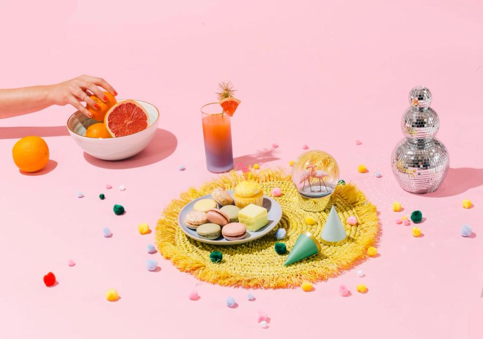 Playful summer styling with pastel pink backdrop, citrus fruits, and whimsical yellow accents creating a cheerful, vibrant mood