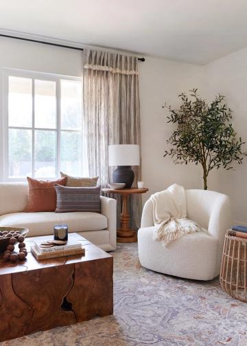 Warm transitional living room with neutral linen curtains, cream curved seating, and rich wood accents creating a sophisticated, inviting atmosphere.