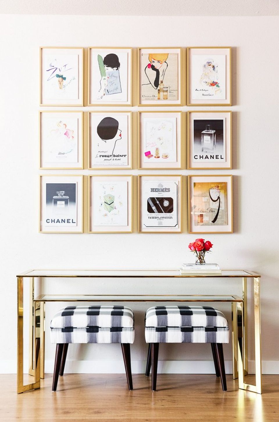 Modern gallery wall with fashion and beauty prints in natural wood frames above a gold console with black gingham ottomans
