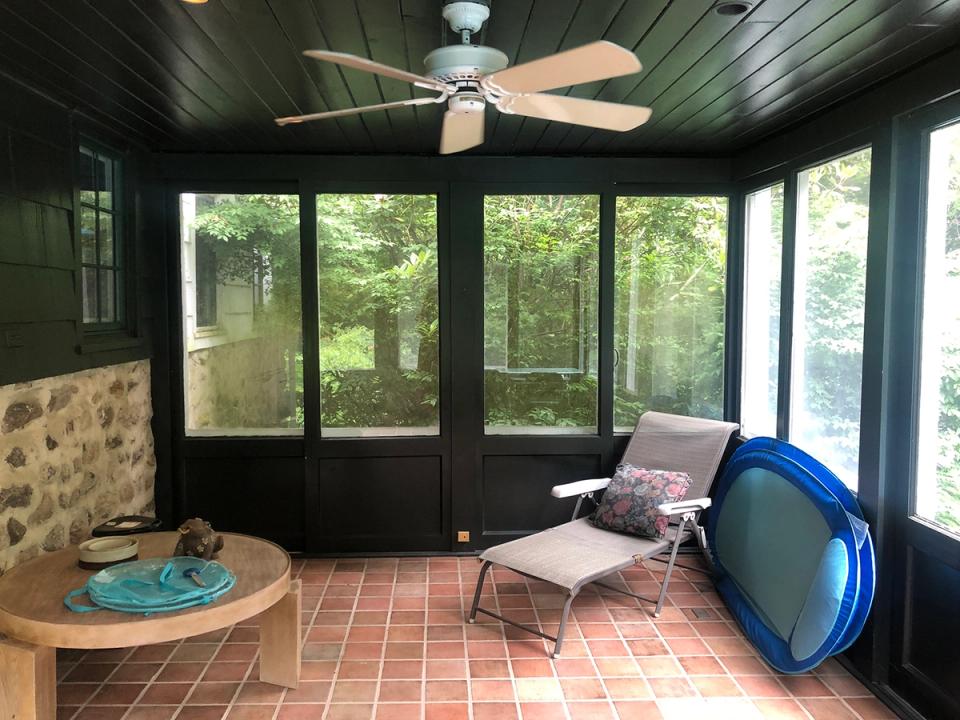 Modern screened porch with dark green walls, natural wood, casual seating, and forest views