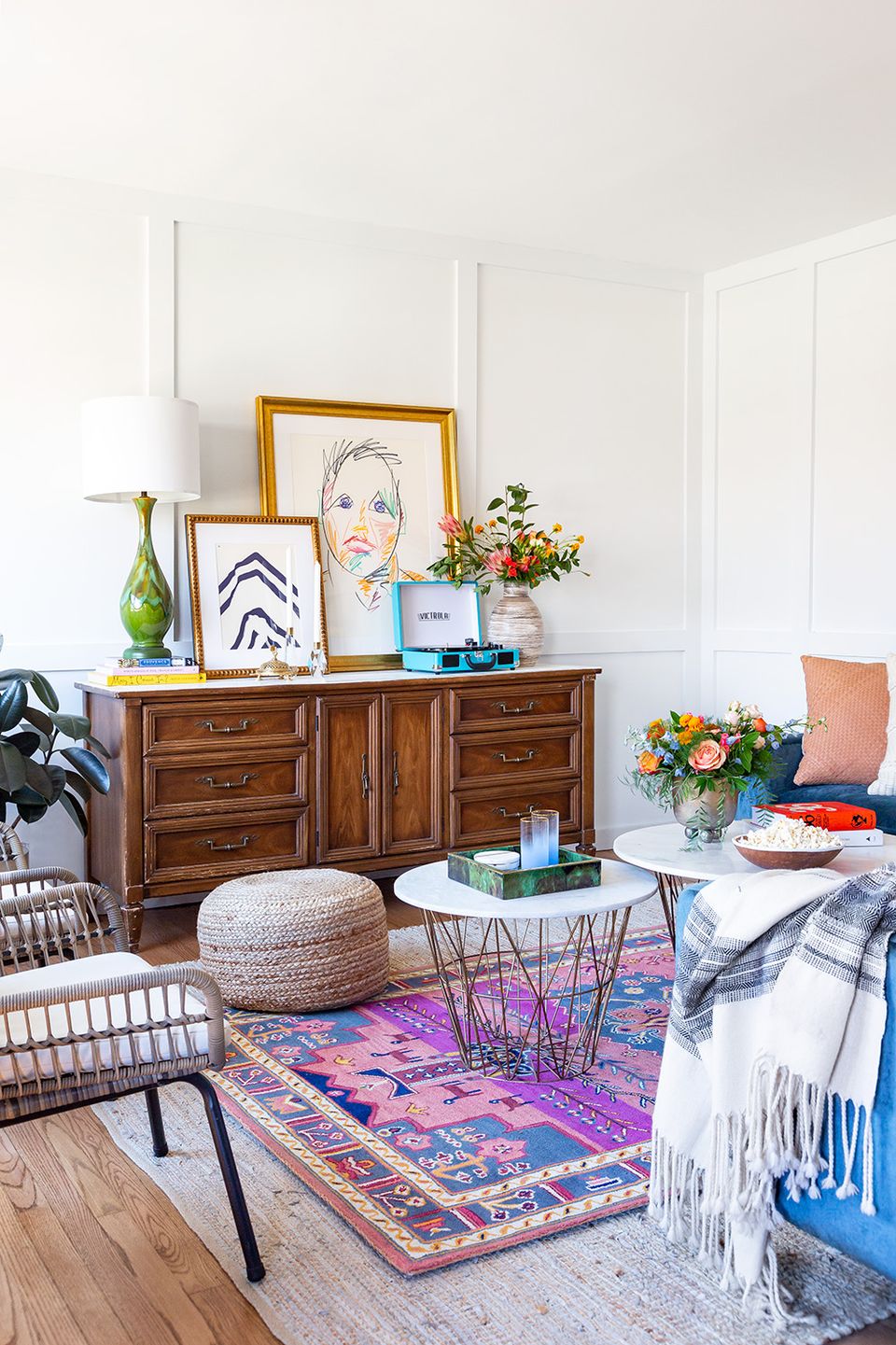 Eclectic living room with jewel-tone patterned rug, warm wood dresser, gallery wall art, and vibrant botanical accents