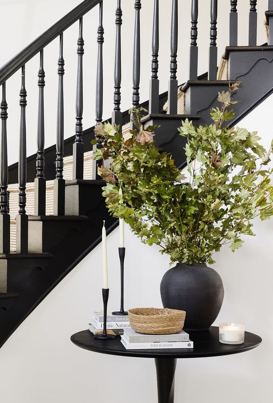 Sophisticated entryway with black staircase, round side table, and statement foliage arrangement