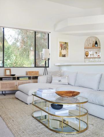 Minimalist modern living room with glass oval coffee table, light blue sectional, and natural wood accents