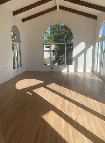 Bright modern sunroom with exposed wood beams, arched windows, natural light, and warm wood flooring in transitional farmhouse style