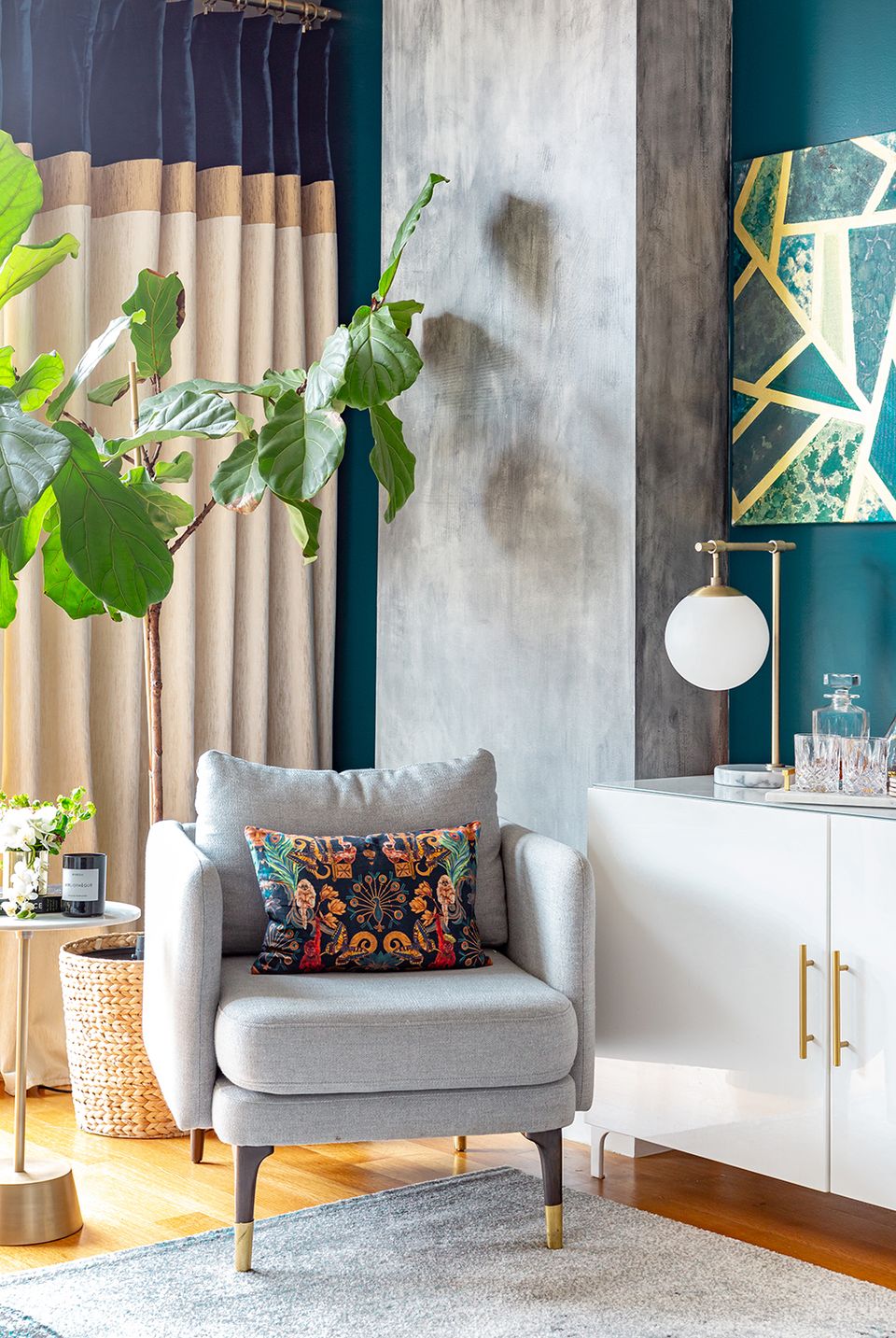 Contemporary reading chair in gray with jewel-tone teal accent wall, botanical elements, and colorful throw pillow.