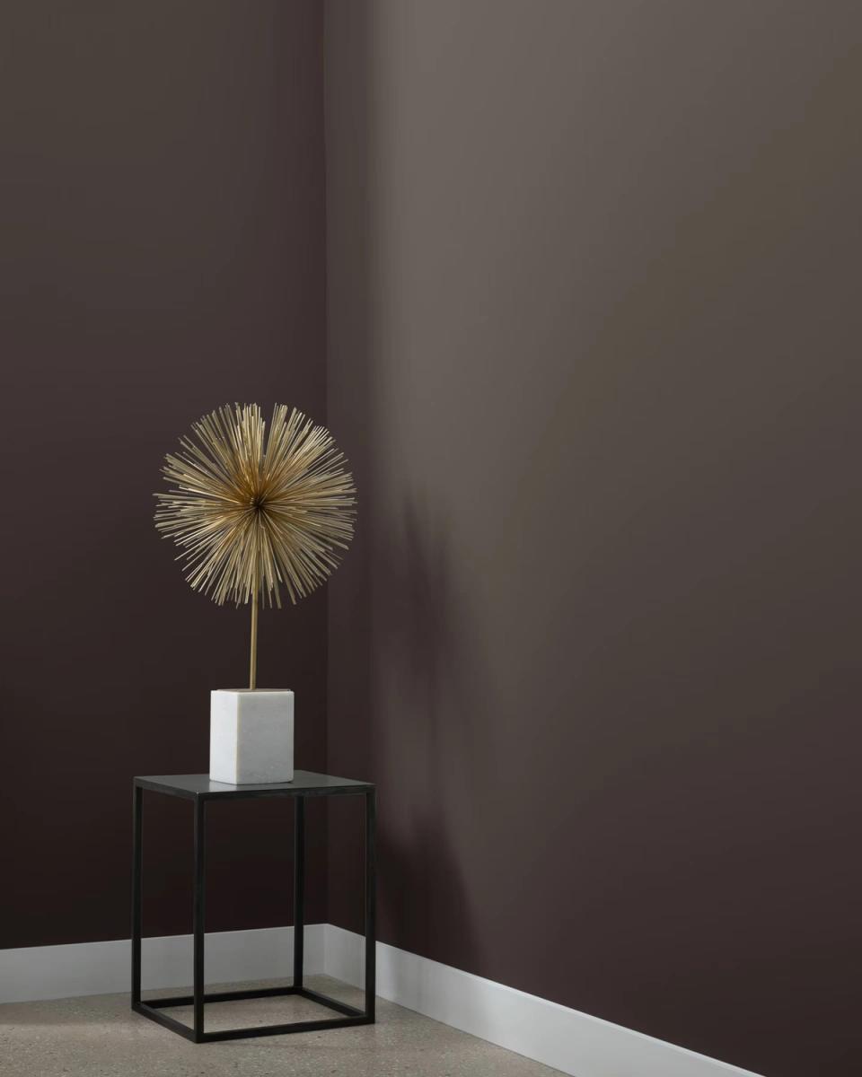 Minimalist dark gray room with brass sunburst sculpture and black metal side table, sophisticated moody aesthetic