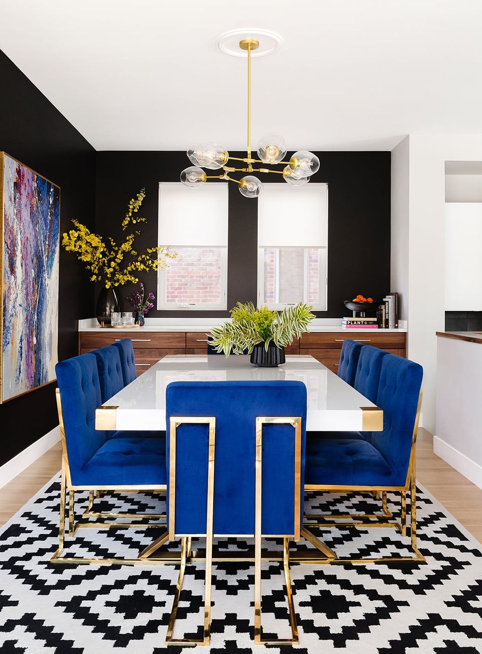 Contemporary dining room with bold black accent wall, cobalt blue velvet banquette, brass accents, and geometric patterns