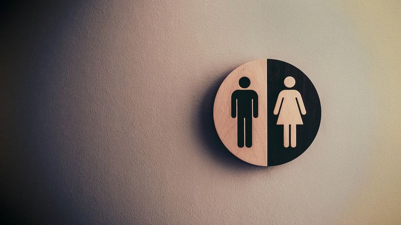 A wooden circular sign divided into two halves, featuring simplified silhouettes of a man on the left and a woman on the right, symbolizing a unisex restroom or gender representation