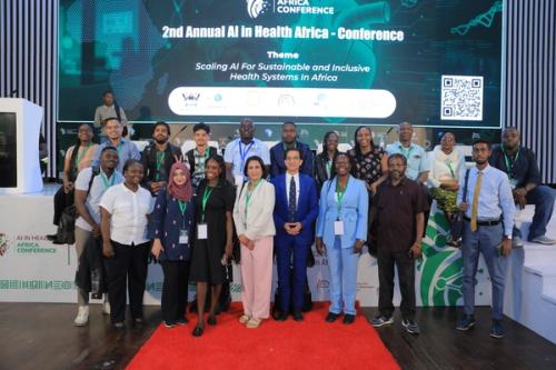 A group of diverse participants from Uganda, Kenya, Nigeria, Nepal, and Pakistan pose together on stage at the 2nd AI in Health Africa Conference after taking part in the Obstetric Ultrasound AI Hackathon. They stand in front of a large conference screen displaying the event theme on AI for sustainable and inclusive health systems.