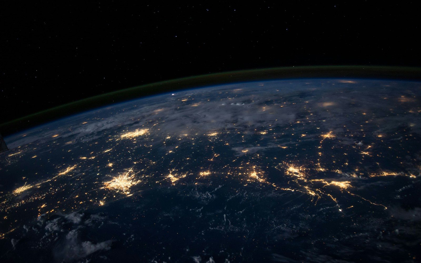 Earth at night viewed from orbit with illuminated cities beneath clouds