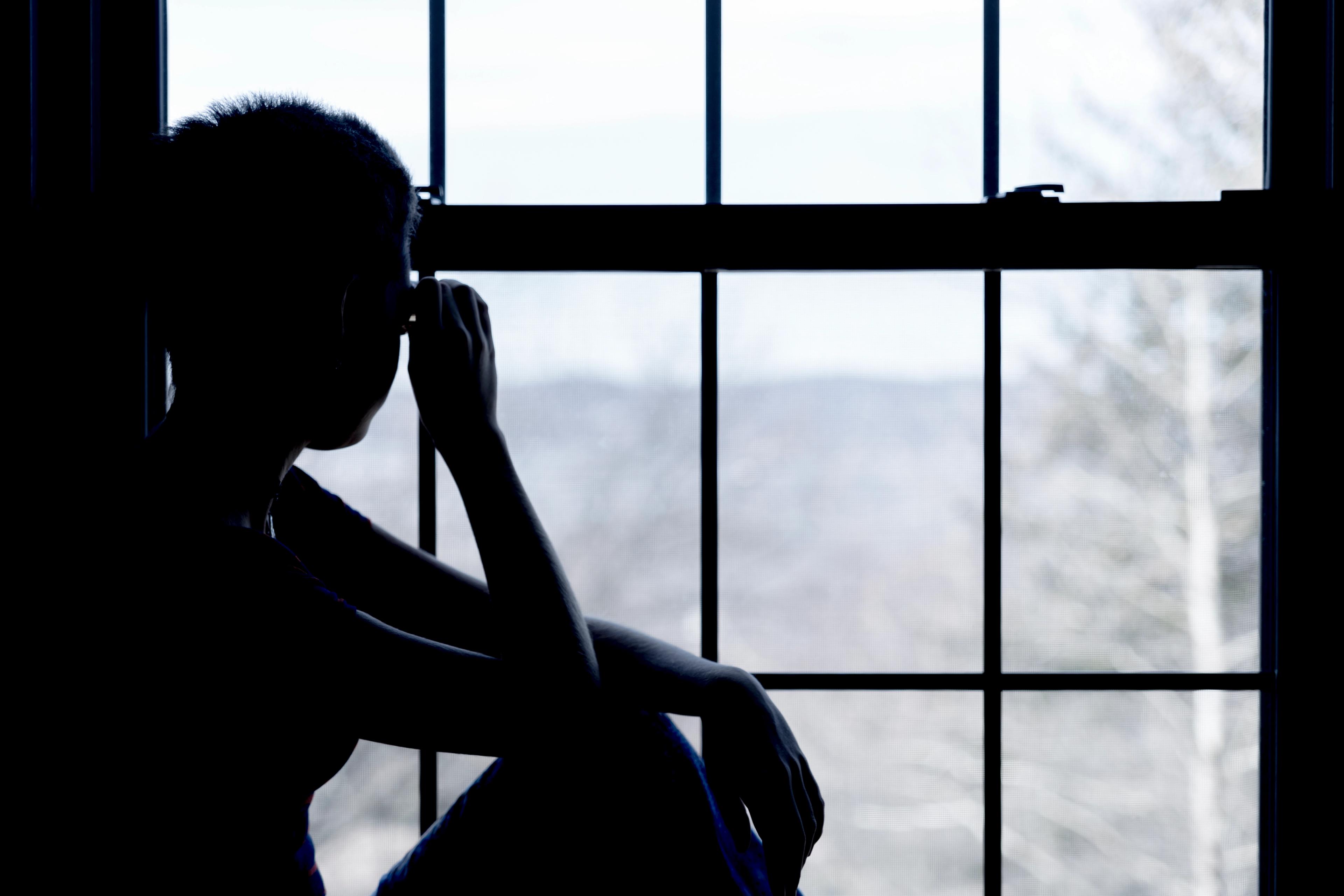 a teenager in silhouette staring out of a window