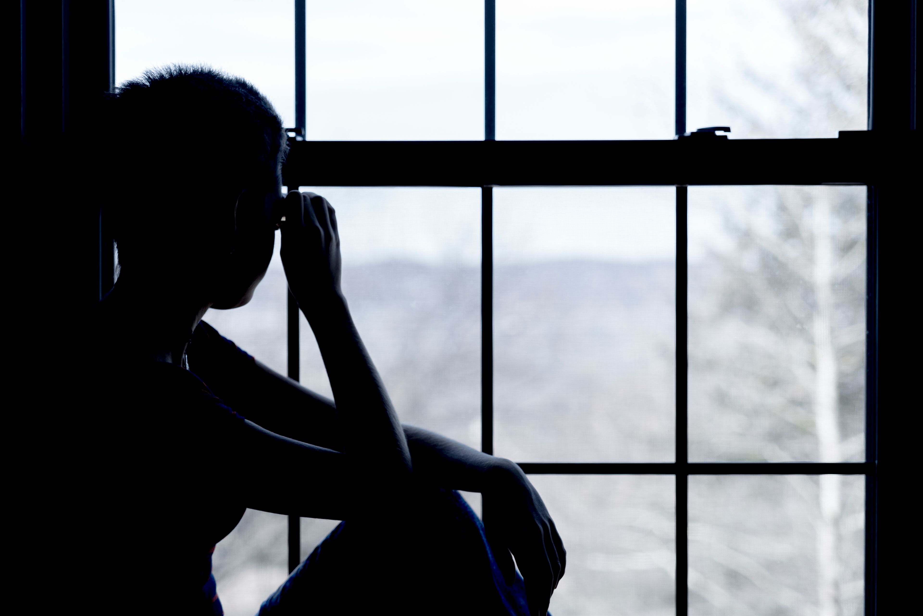 a teenager in silhouette staring out of a window