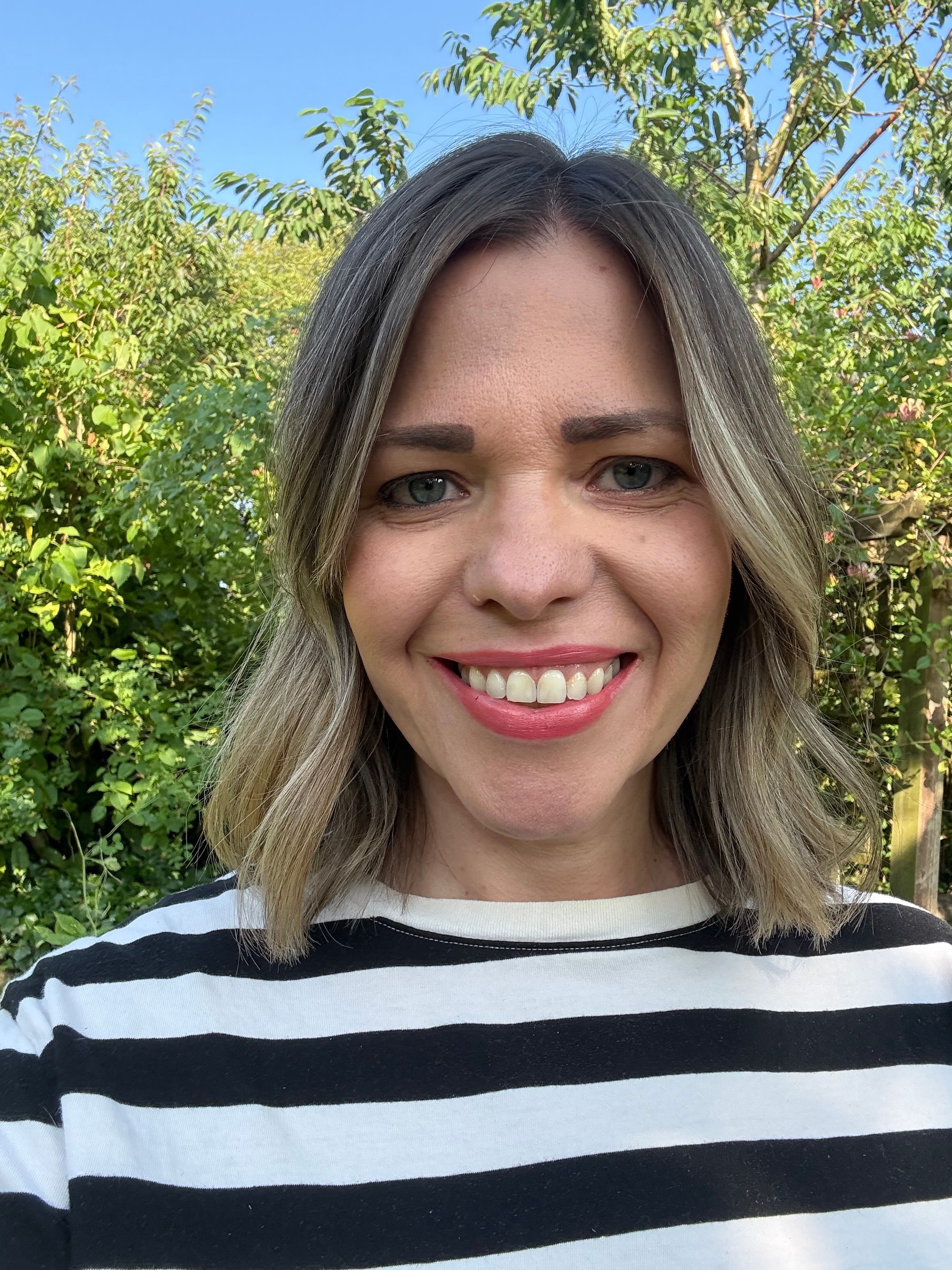 Finding Therapy counsellor Helen Spiers, smiling outdoors in front of a garden hedge