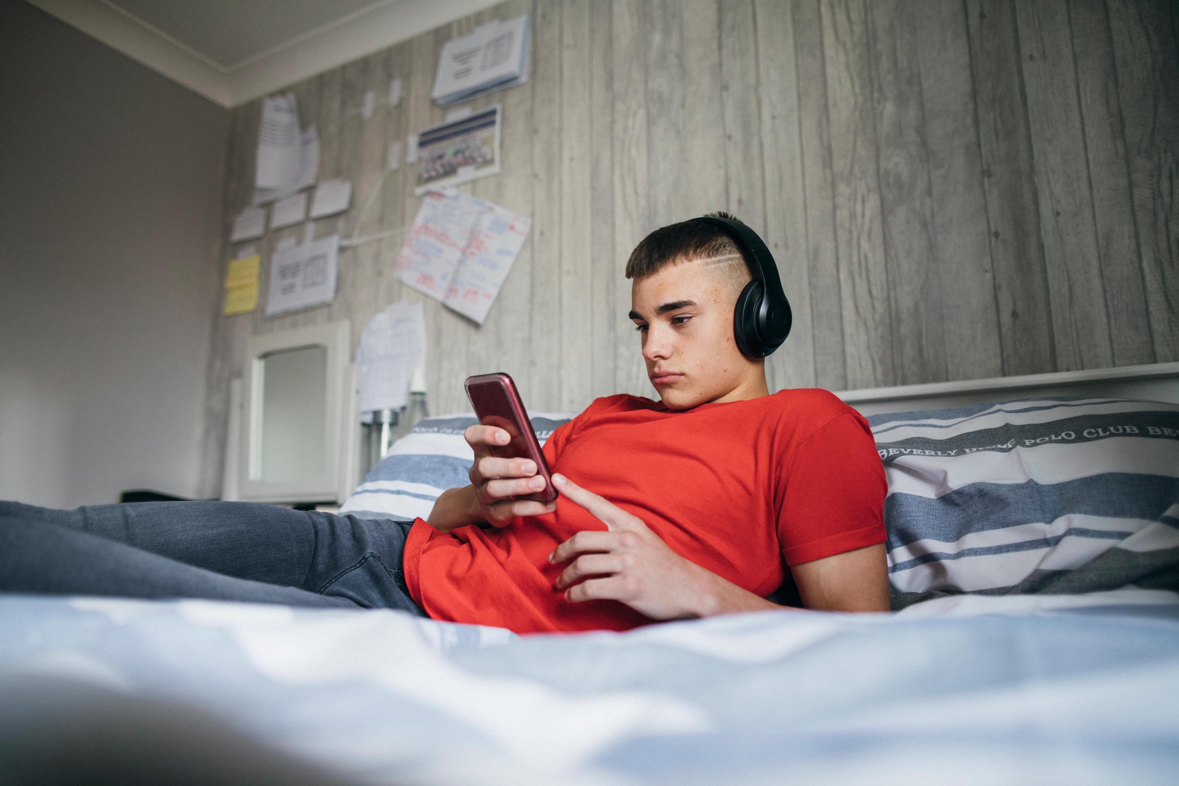 A teenager sits on their bed looking depressed