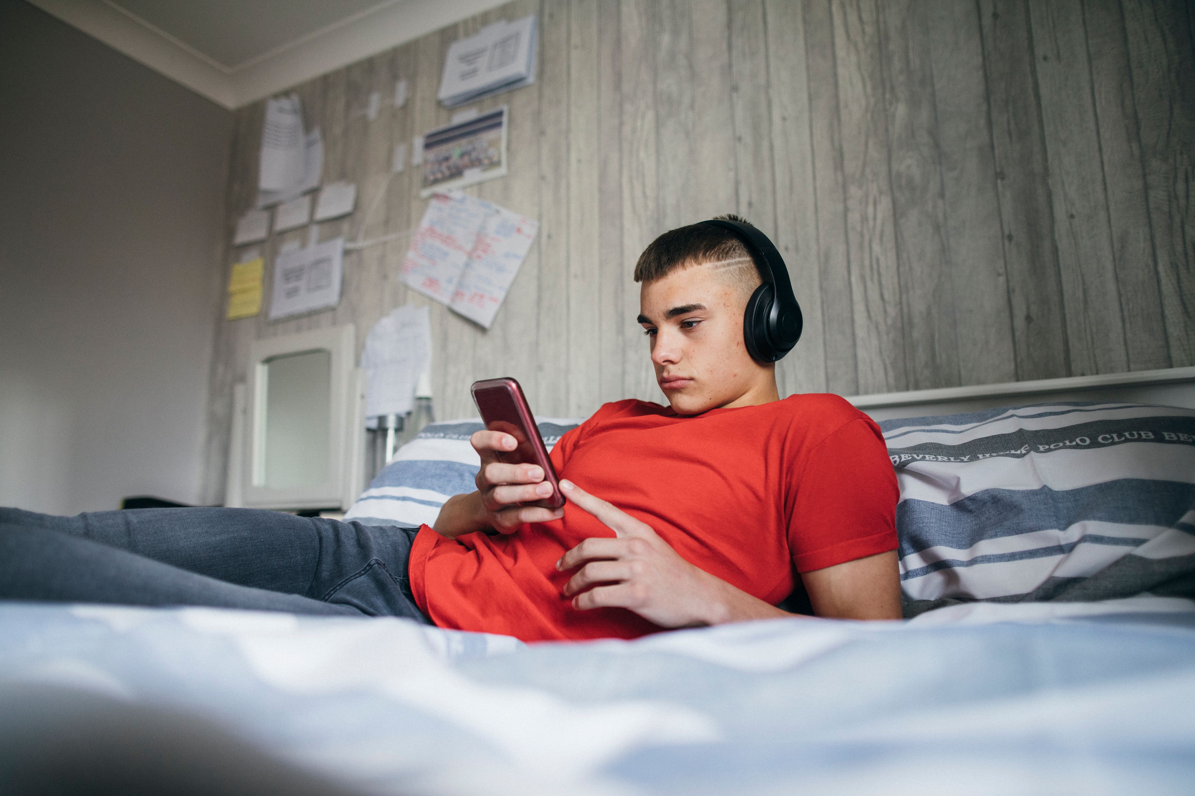 A teenager sits on their bed looking depressed