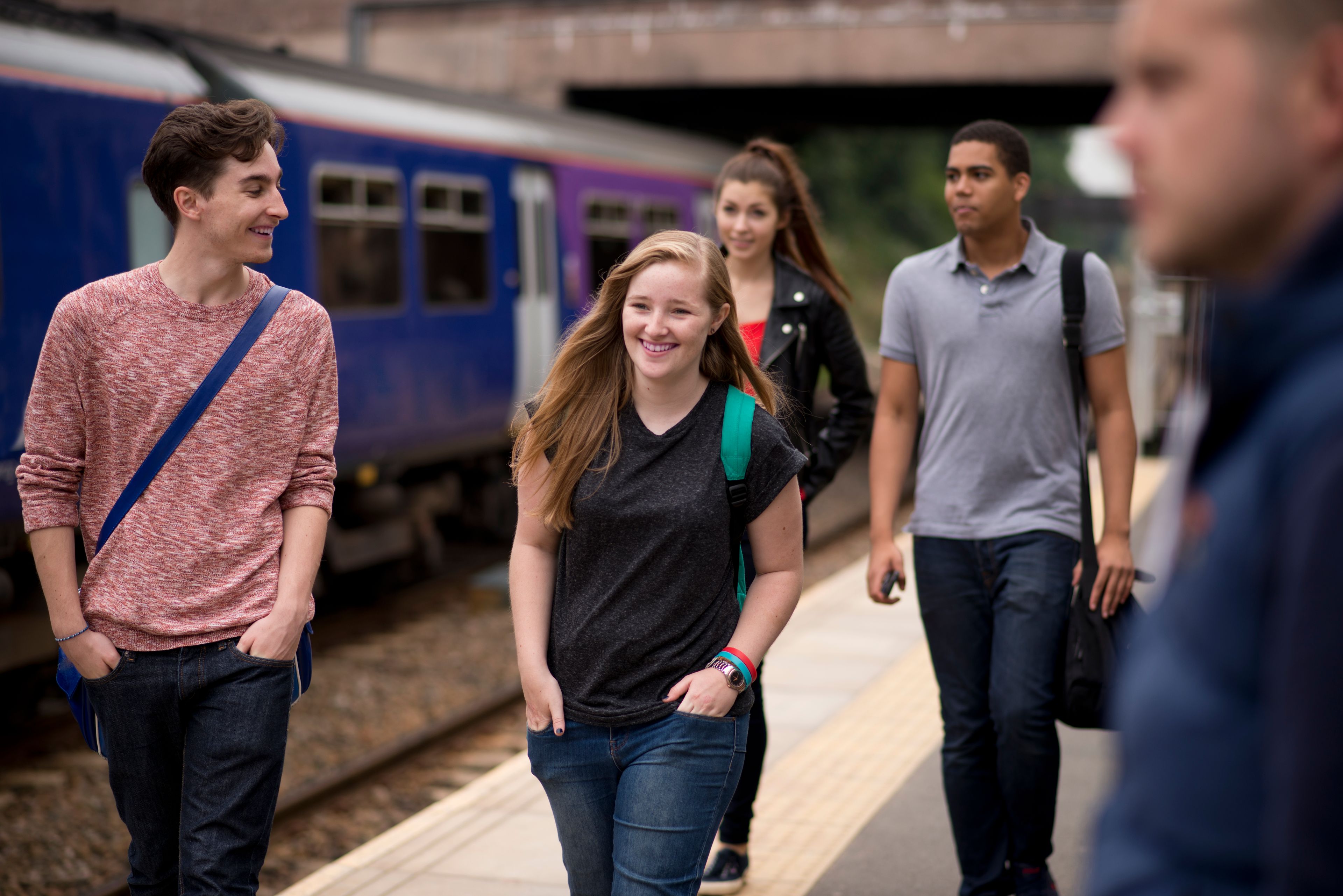 Smiling young people walking on a train platform.