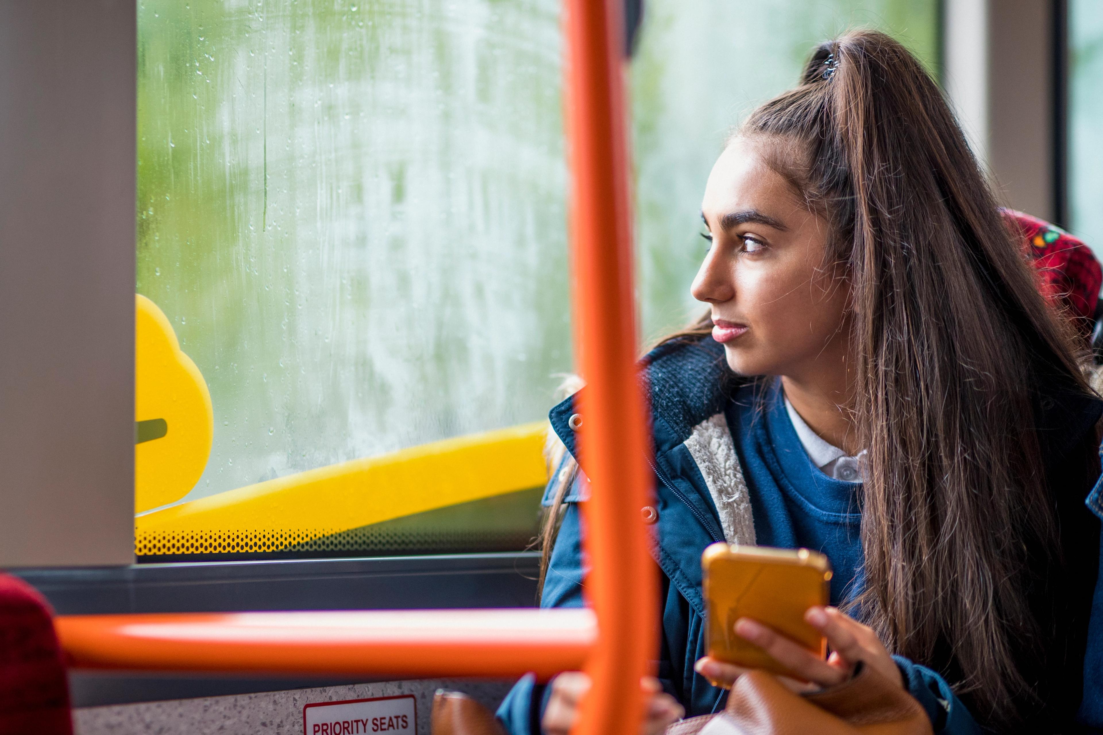 A teenage girl sits on a bus staring out of the window