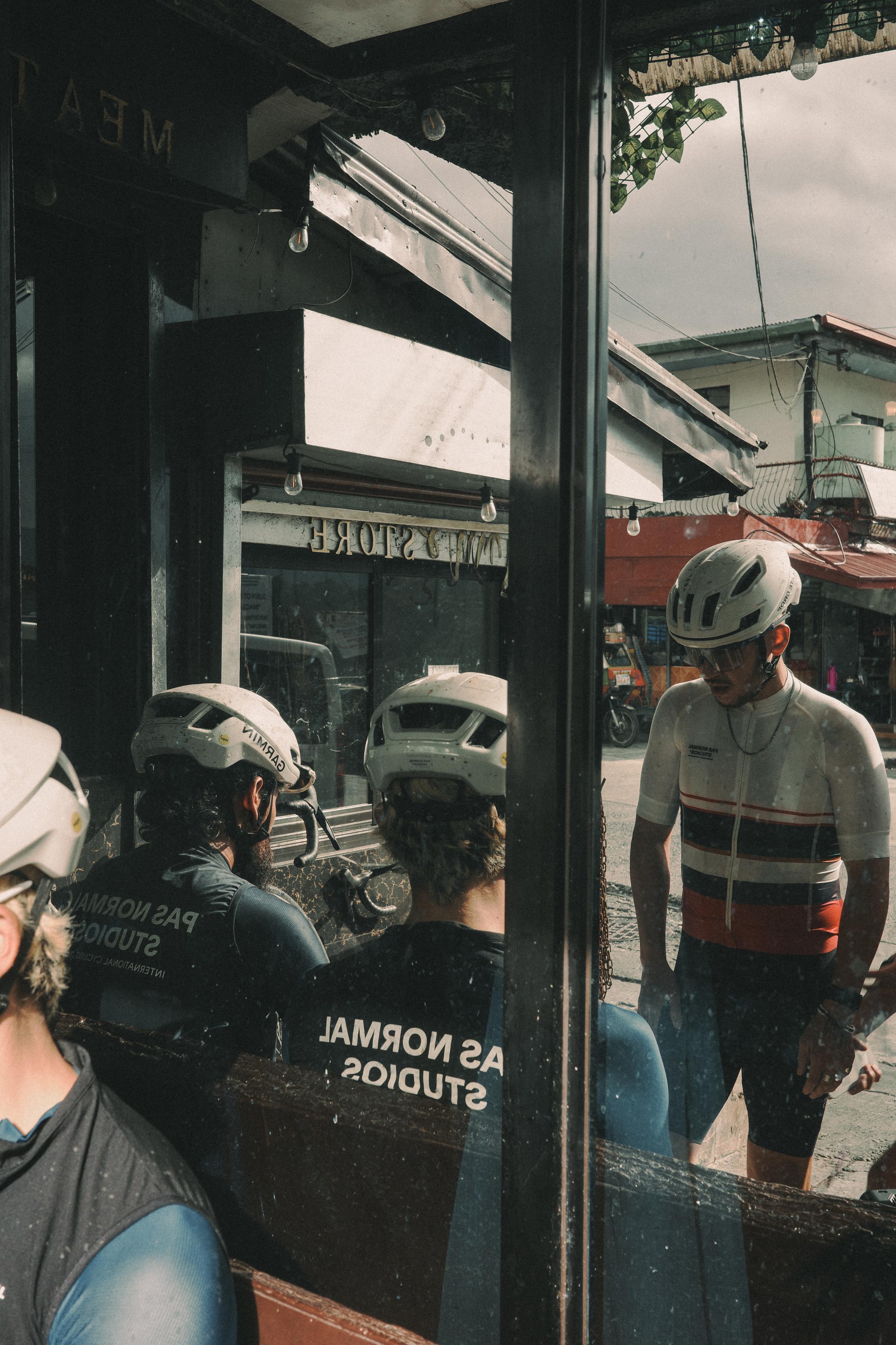 Cyclists in helmets and cycling apparel reflected in cafe window, urban street setting