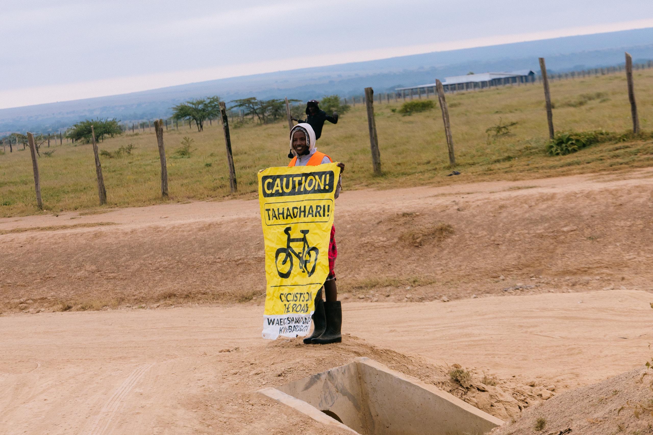Model holding yellow caution sign on rural dirt road in open countryside