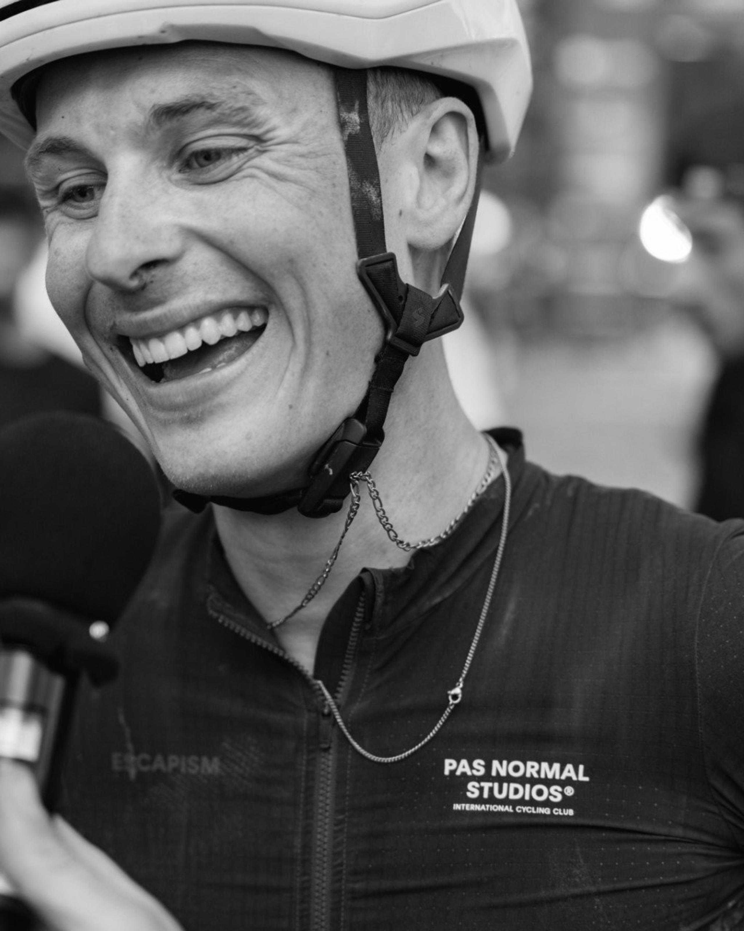 Model wearing cycling helmet and dark jersey with chest branding, smiling in black and white portrait