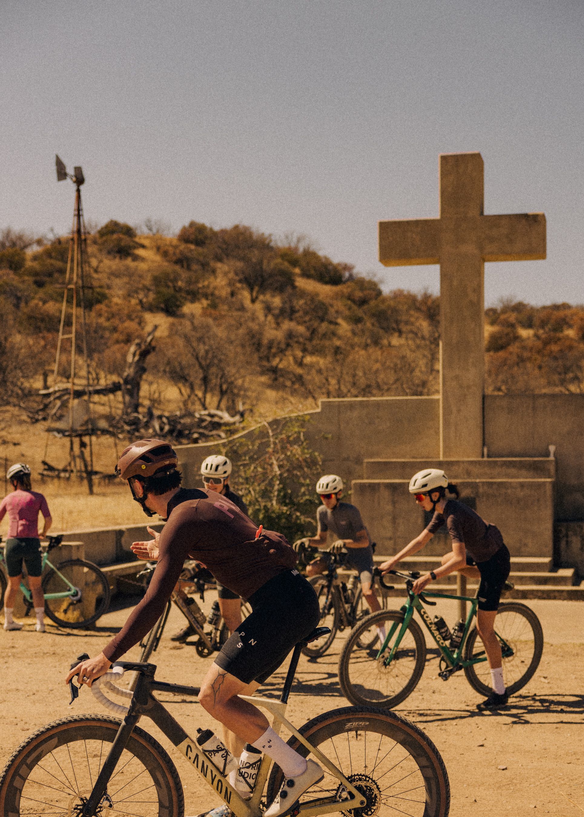 Cyclists training on gravel bikes in desert landscape with cross monument