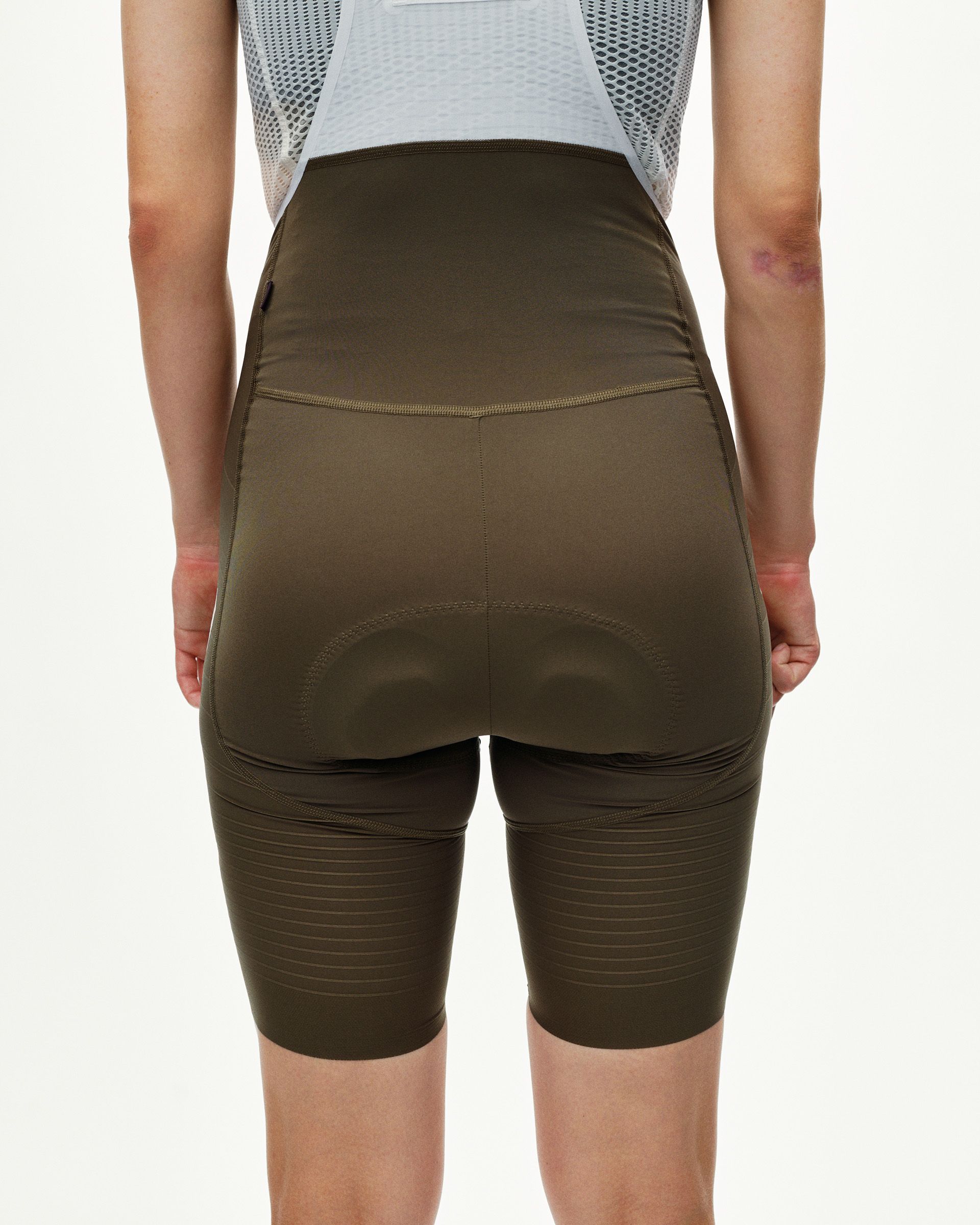 Dark Earth khaki PAS Mechanism Pro women's cycling bibs on model, rear view with horizontal ribbed leg panels