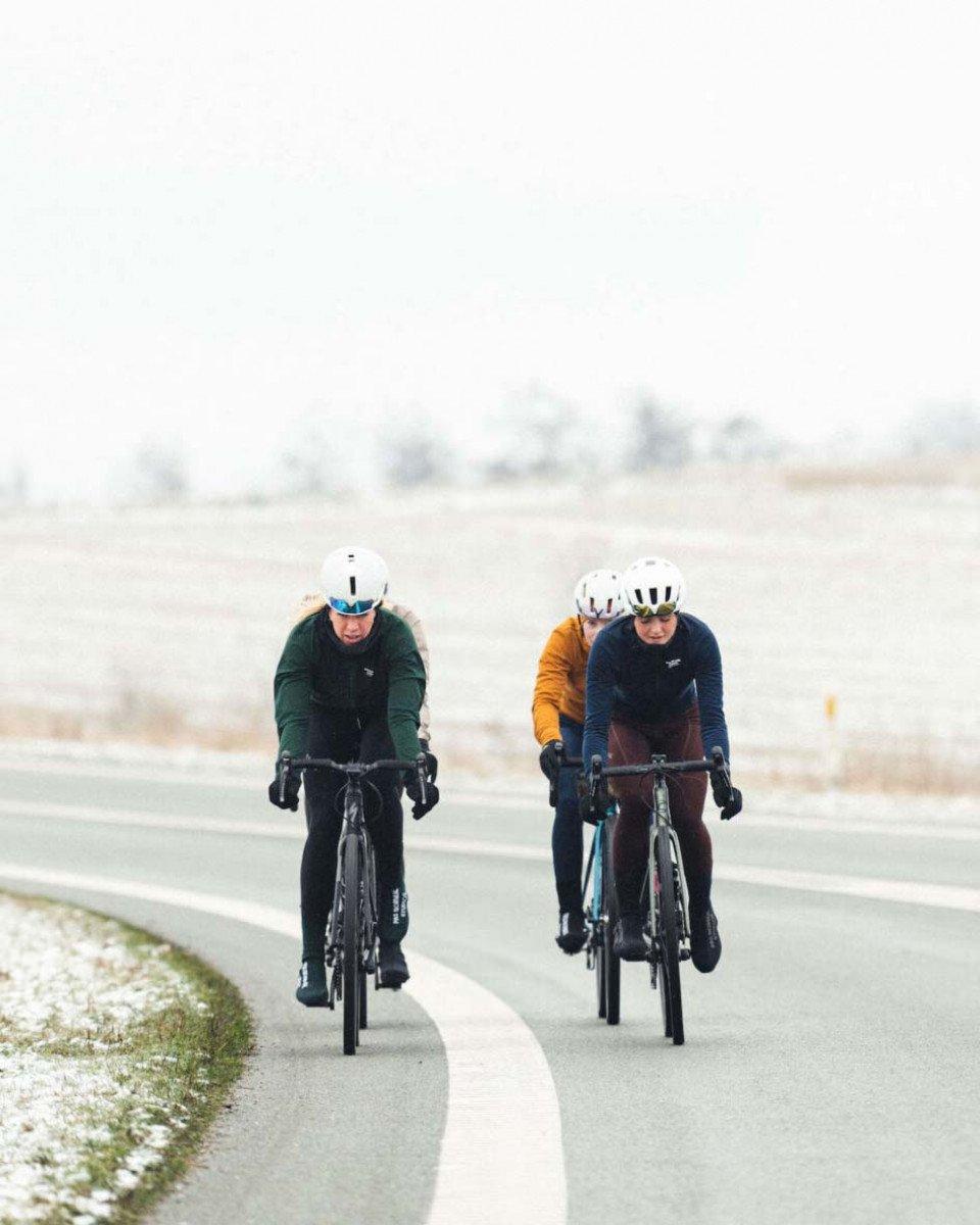 Two cyclists in aerodynamic positions on time trial bikes wearing colorful winter cycling apparel on snowy road
