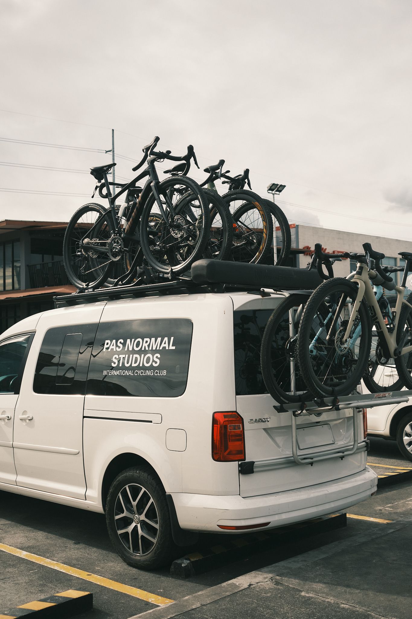 White support van with cycling team branding carrying multiple road bikes on roof and rear racks