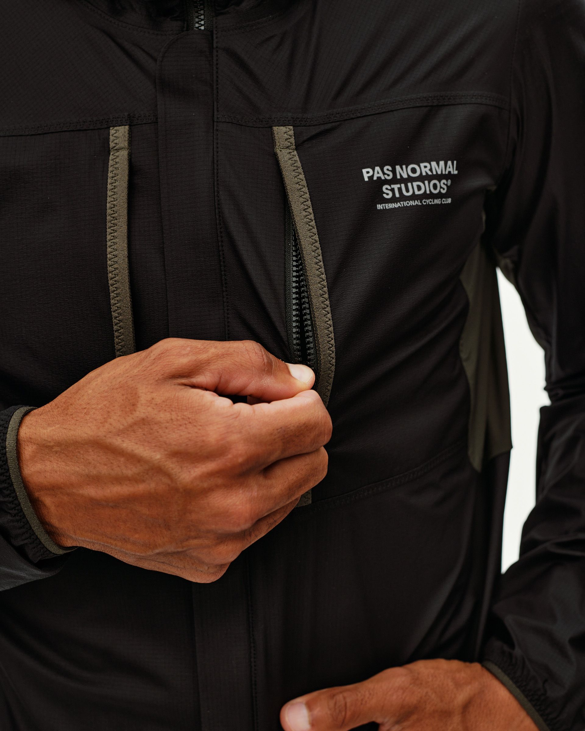Black Escapism Hooded Lightweight cycling jacket, front detail on model with olive zip pulls and reflective sleeve panel
