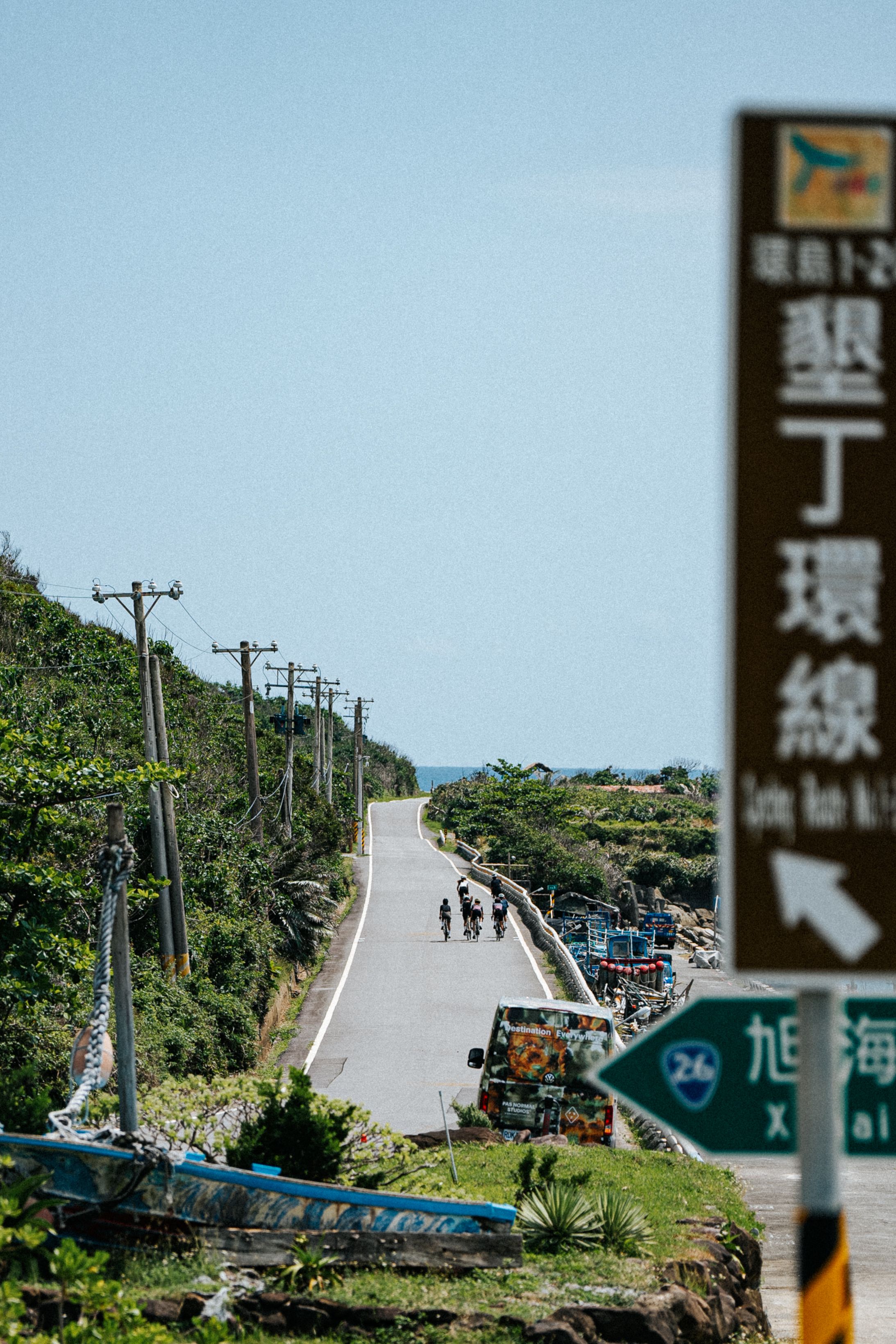 Cyclists on coastal road with tropical vegetation and road signs