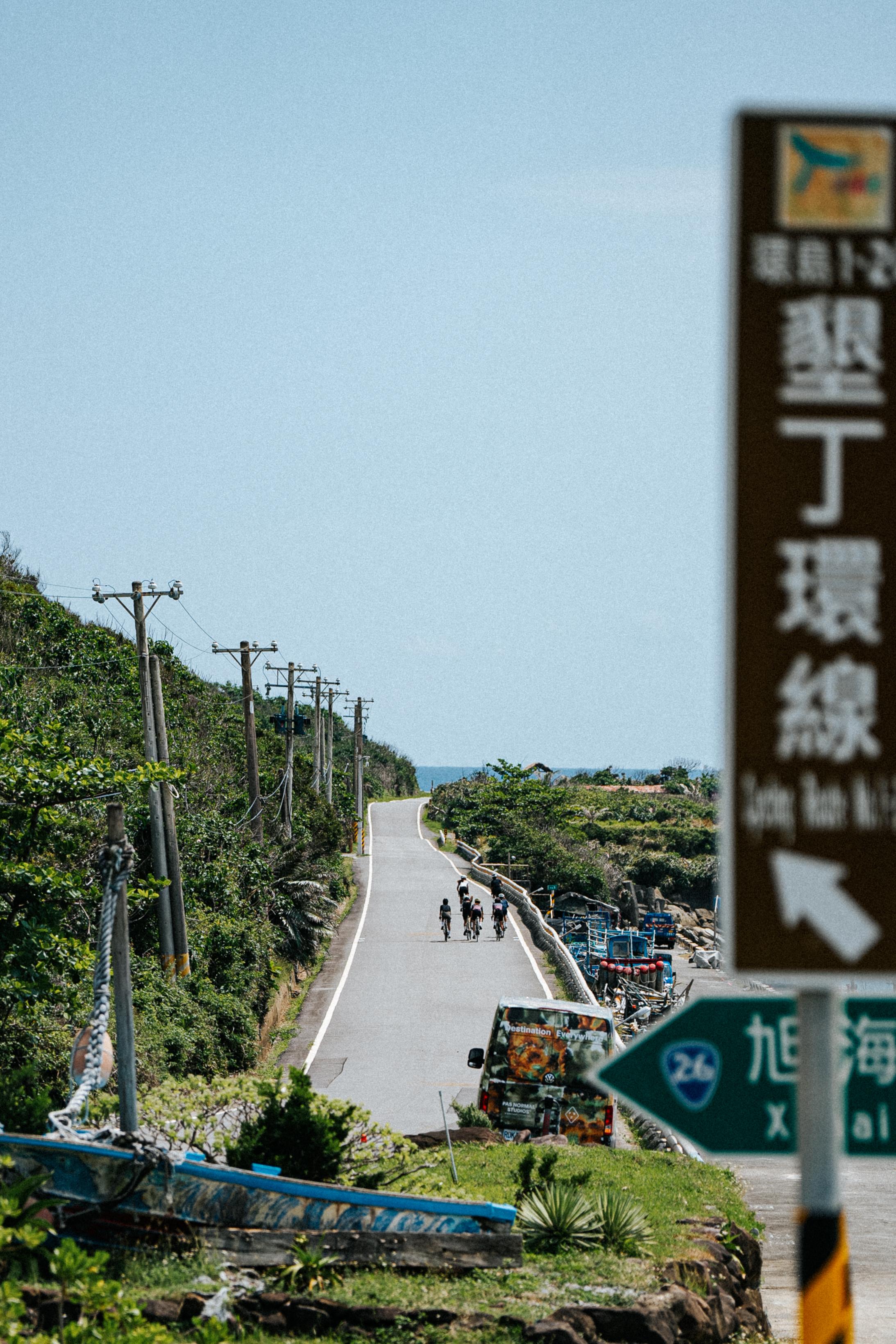 Cyclists on coastal road with tropical vegetation and road signs