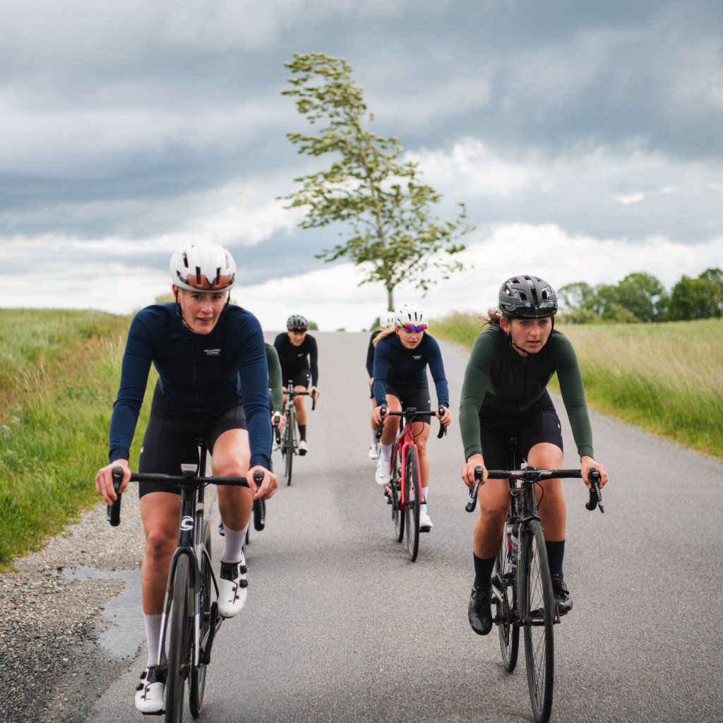 Four cyclists in aerodynamic position on time trial bikes riding on country road through rural landscape