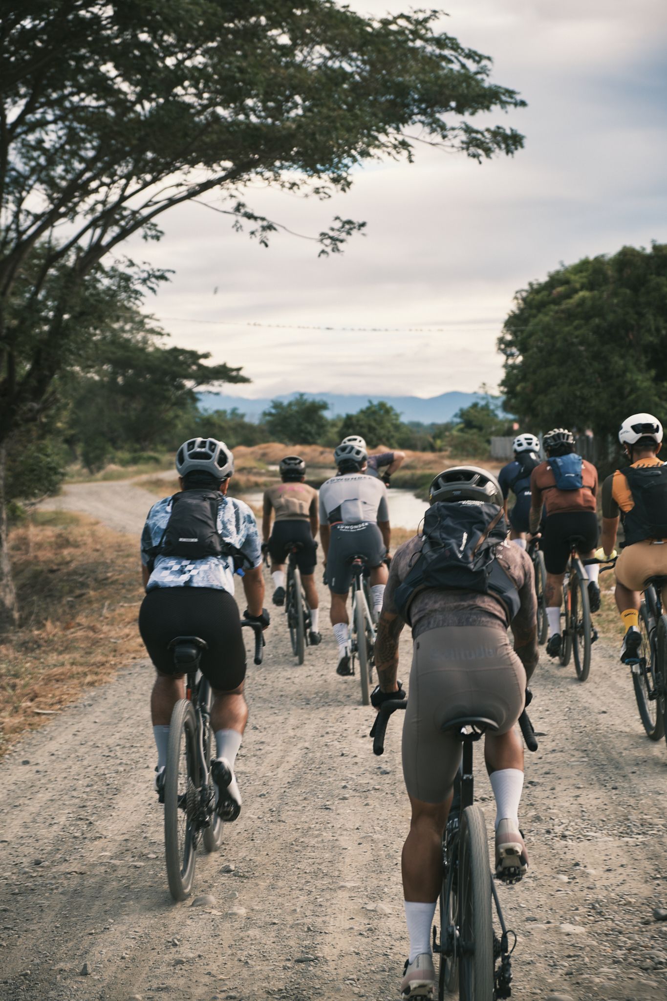 Group of cyclists riding on gravel road through countryside landscape at dusk