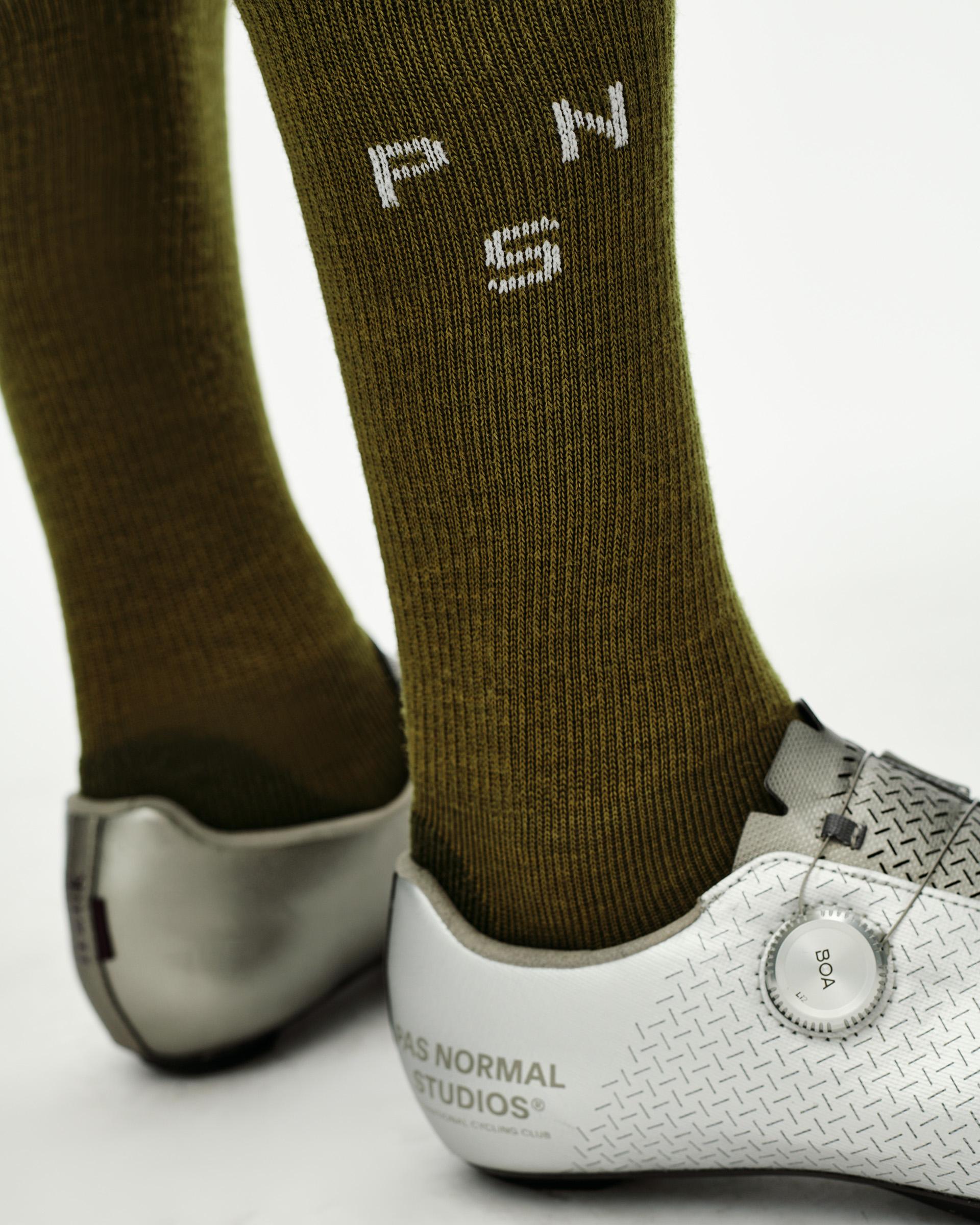 Khaki Green Deep Winter Wool cycling socks on model, detail view with white woven logo on calf