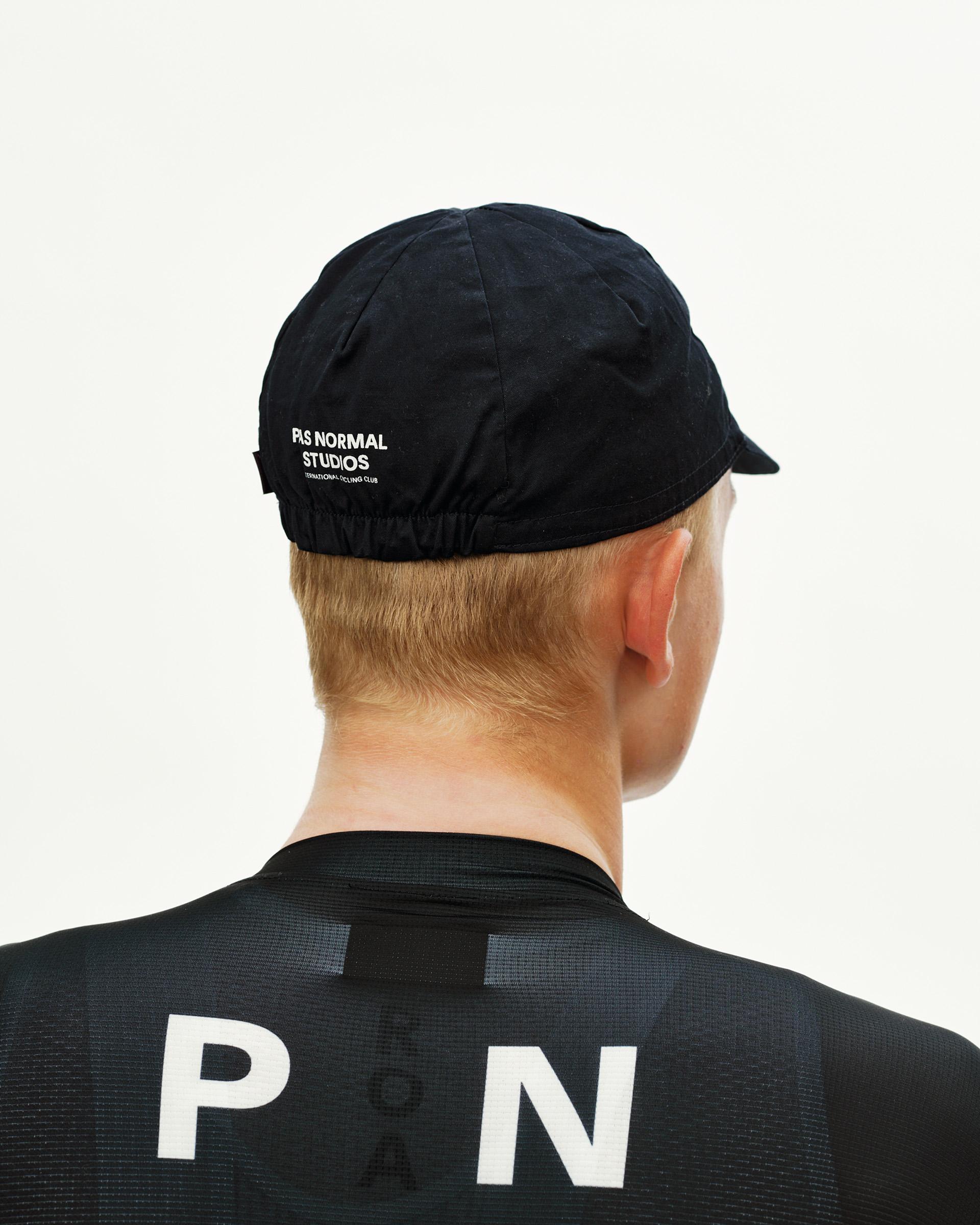 Black Logo Cap cycling cap, rear view on model with white logo print and elastic hem
