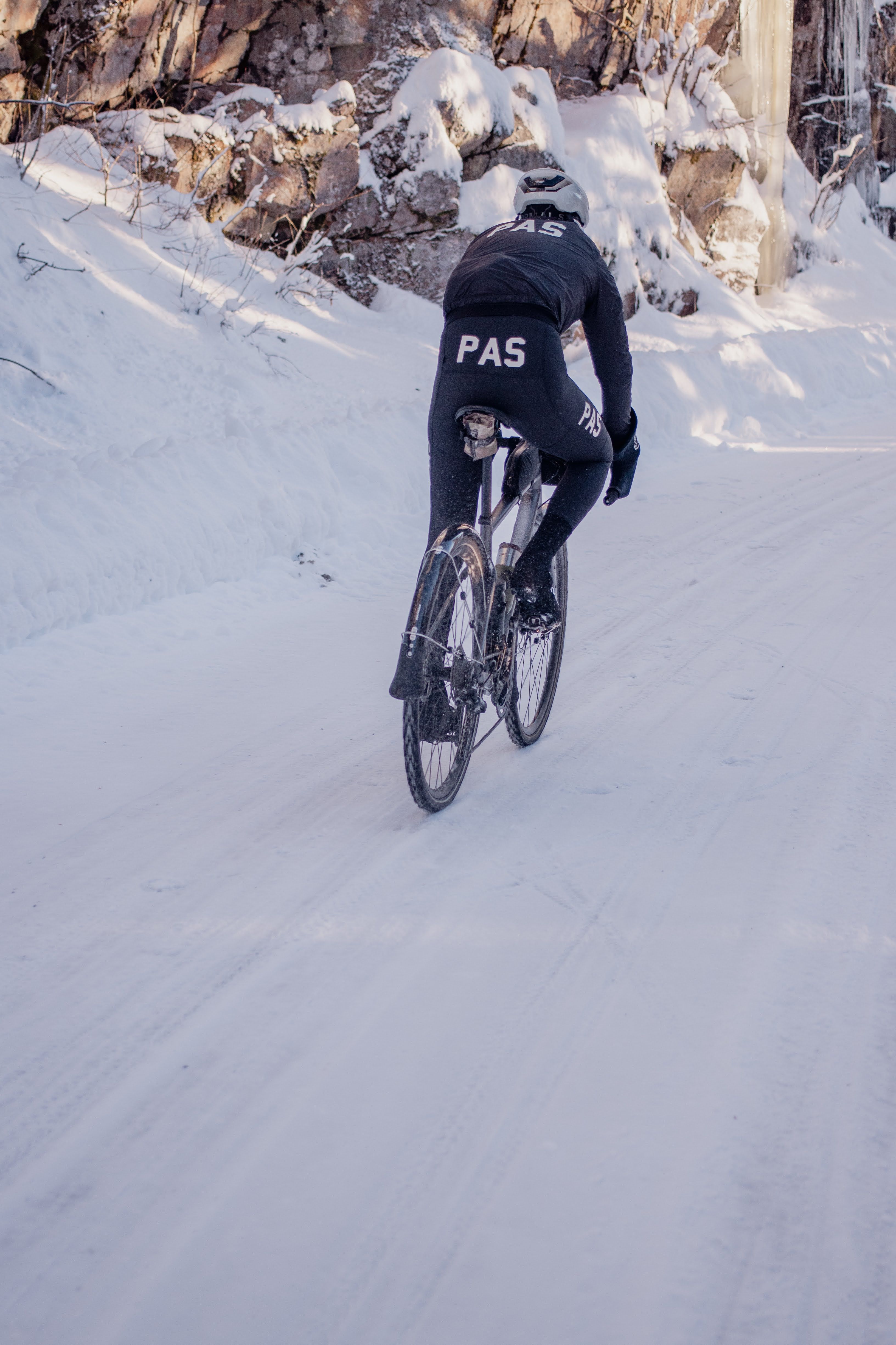 Model wearing black PAS collection jersey cycling in snowy mountain terrain