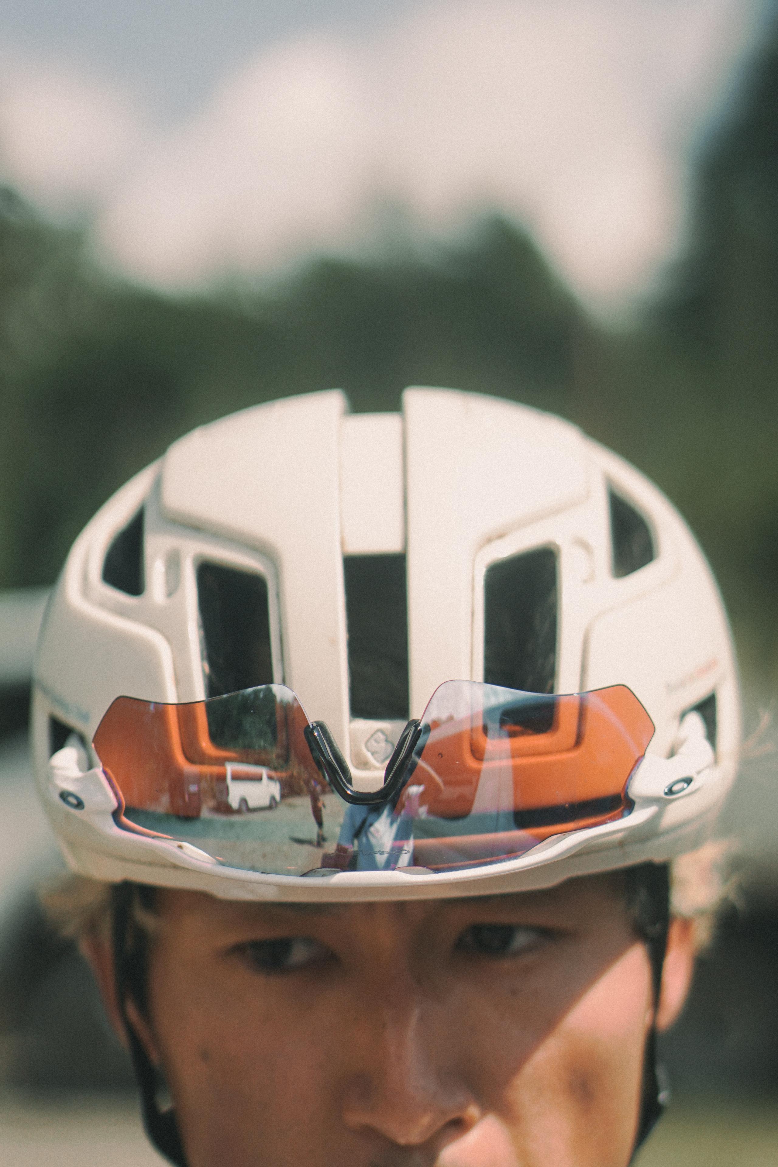 Model wearing white cycling helmet with orange-tinted sunglasses outdoors
