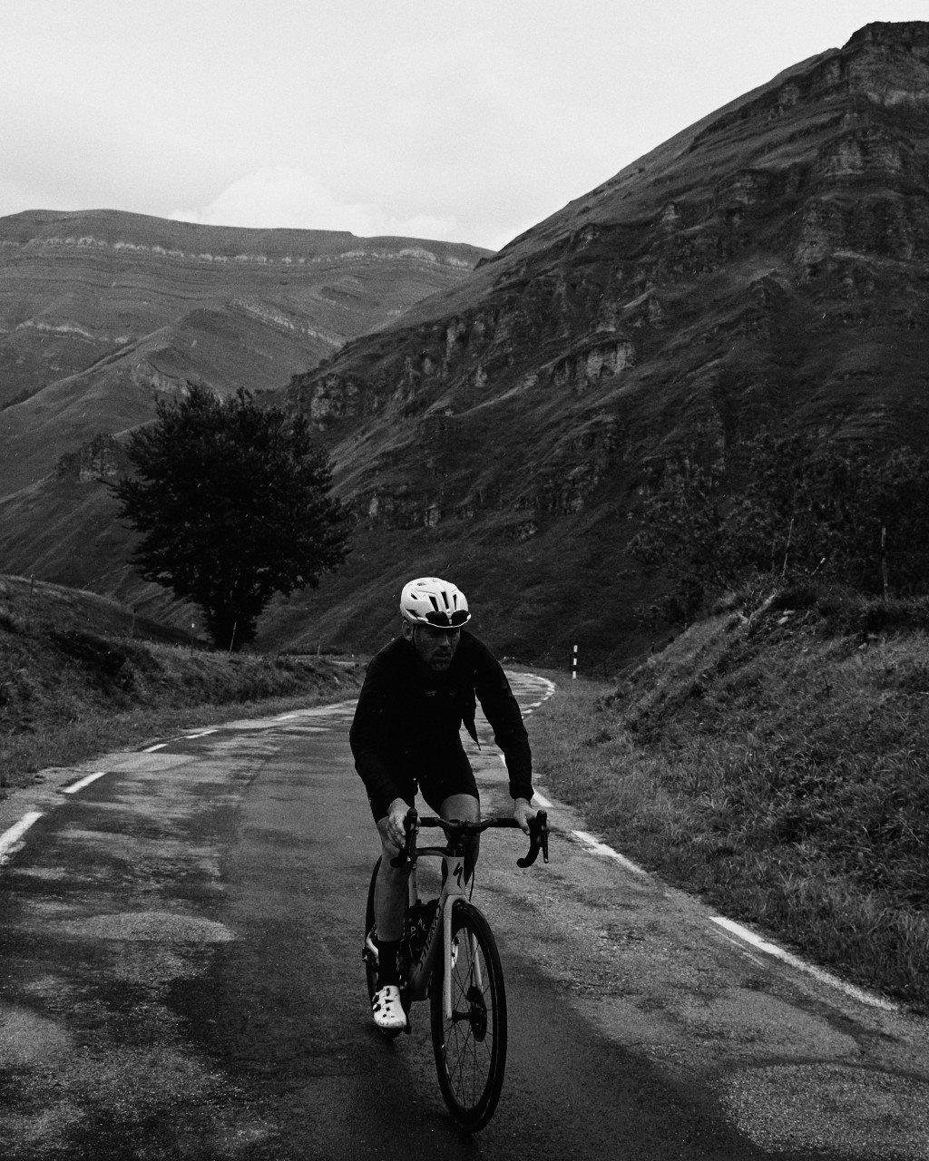 Model wearing black cycling apparel on mountain road in hilly landscape, black and white photography