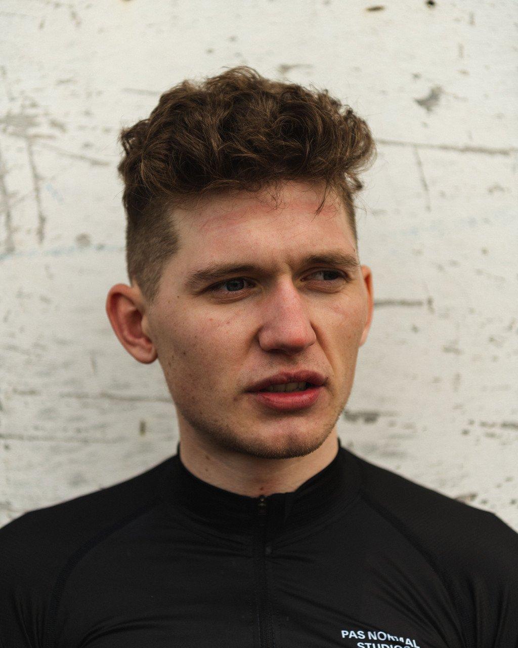 Model wearing black cycling jersey with logo branding against white brick wall