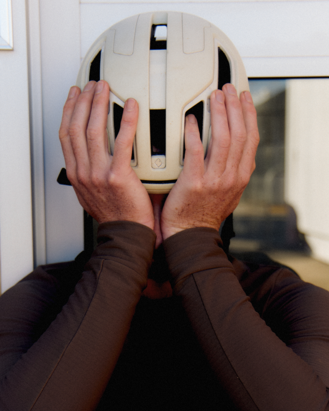 Hands cupping white cycling helmet with ventilation openings in indoor setting