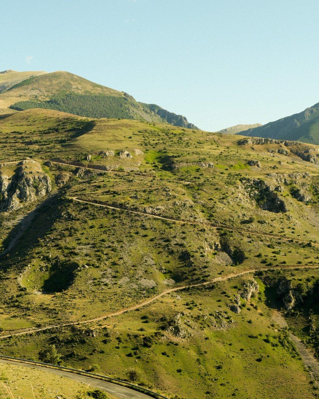 Winding mountain road through rolling green hills and valleys under clear blue sky